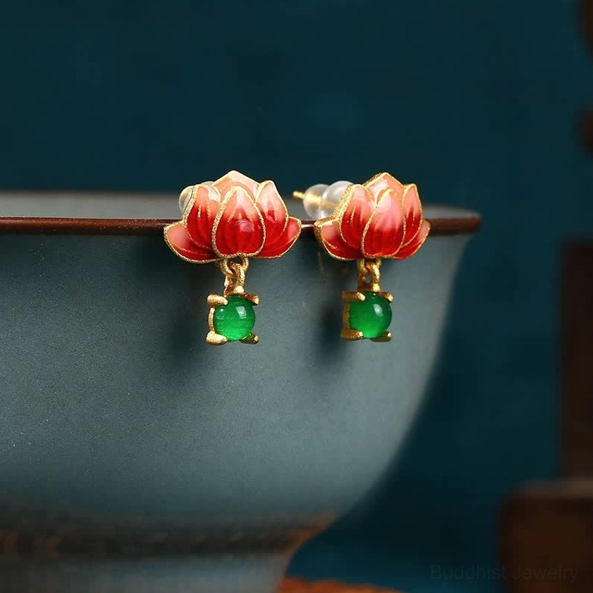 Red lotus enamel dangle earrings with green jade charm, displayed on dark blue ceramic rim, showing side close-up of gold-tone metal work and cloisonné lotus design