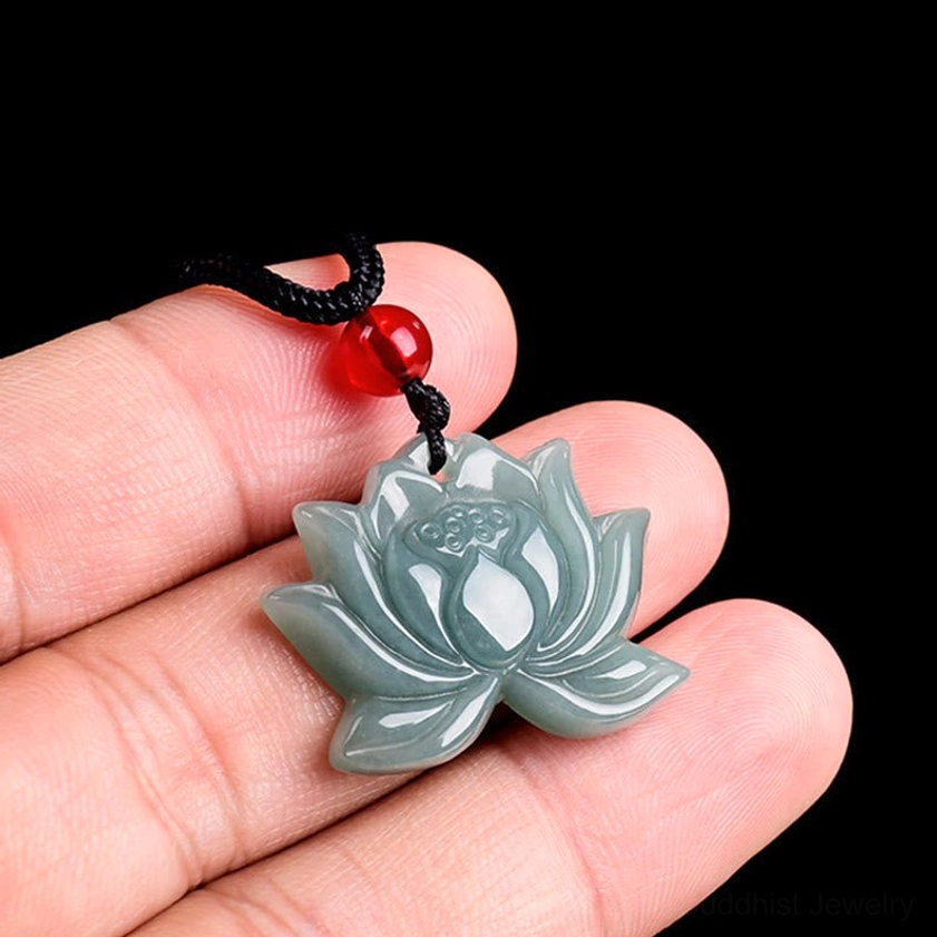 Carved lotus jade Buddhist pendant held between fingertips showing celadon tone and red accent bead close-up