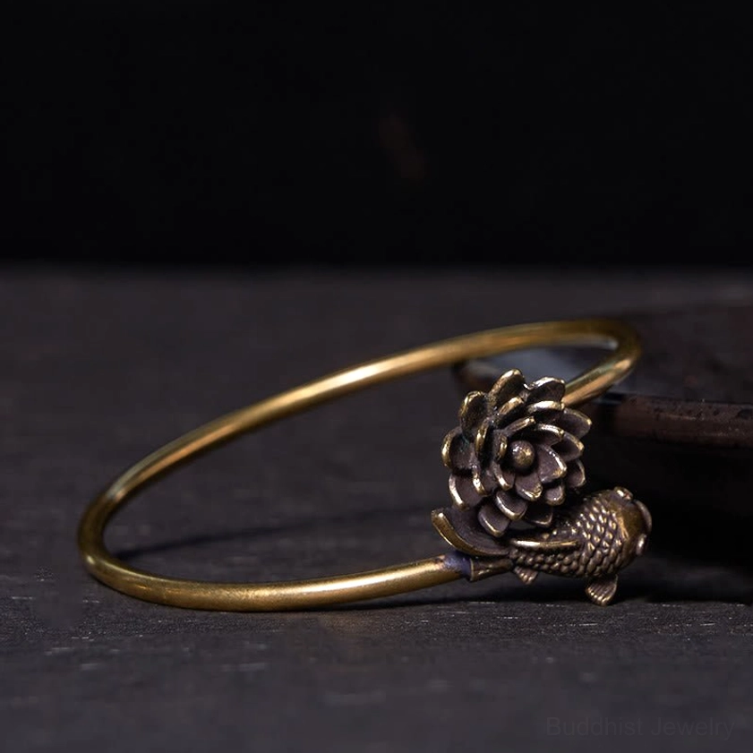 Handmade antiqued brass lotus koi fish bangle from low angle view on wooden background, showcasing detailed embossed lotus and koi ornament