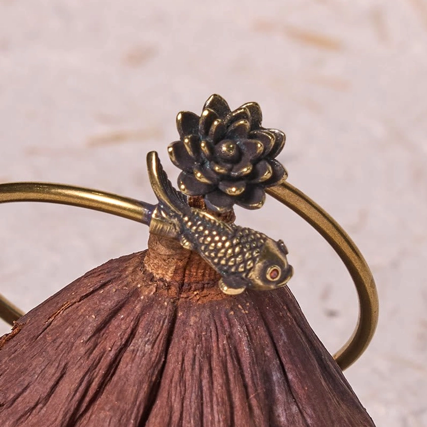 Buddhist lotus koi copper bangle bracelet top oblique view on dried lotus pod background, featuring 3D carved lotus and koi decorative charms