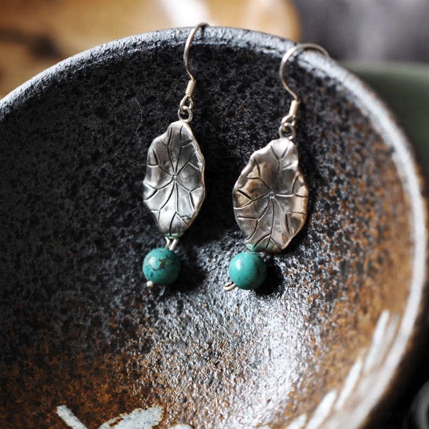 Two-tone sterling silver lotus leaf earrings with paired turquoise stones in ceramic bowl