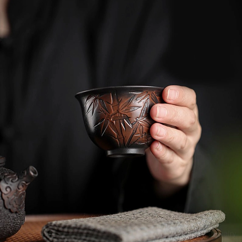Side profile of ceramic tea cup showing embossed lotus and leaf patterns with rounded bowl silhouette