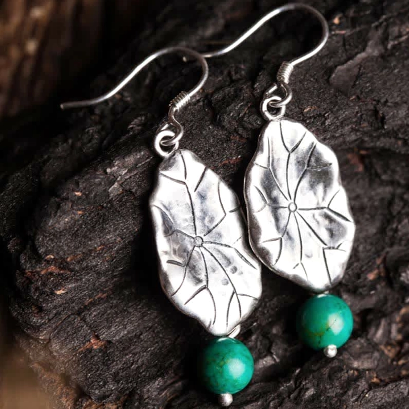 Top-down view of turquoise and silver lotus leaf dangle earrings showing carved details