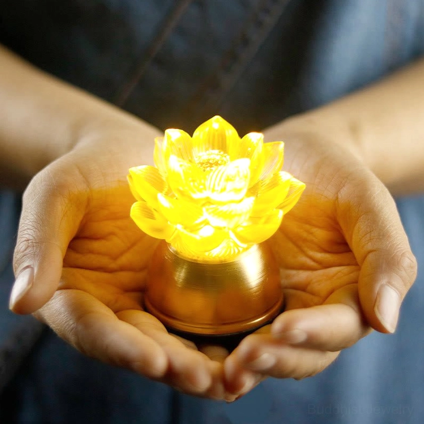 Warm glowing yellow lotus liuli glass prayer light with rose-gold copper base held in hands, close-up handheld view