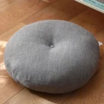 Dark gray linen lotus meditation seat cushion with central button tufting, overhead view on wooden floor