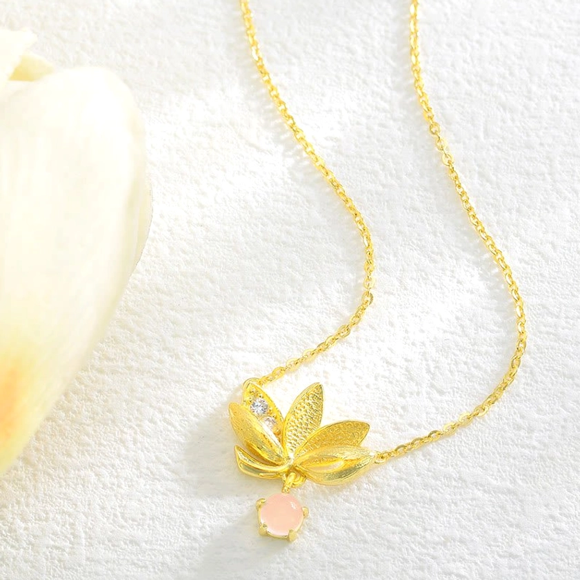 Gold plated lotus pendant necklace flat lay on white fabric with decorative tulip styling shot