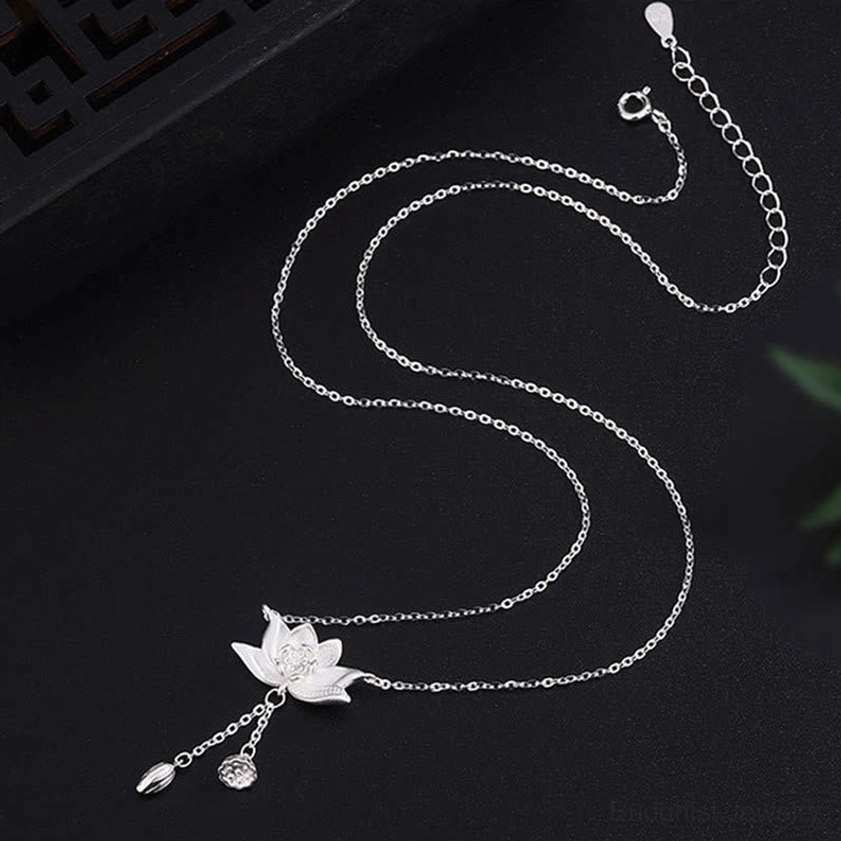Flat lay overhead view of silver lotus tassel necklace with curved fine chain on dark studio background