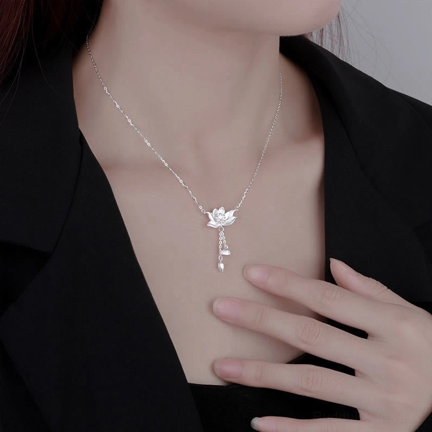 Sterling silver lotus pendant necklace held in hand with sheer beige sleeve, showing scale and elegance on wooden background