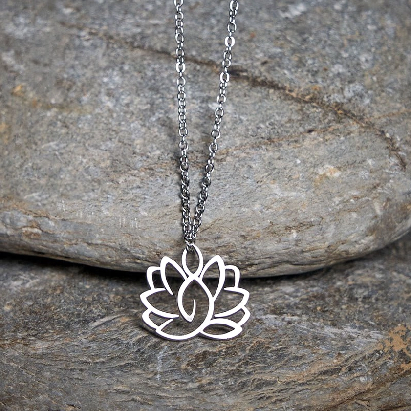 Silver lotus Buddhist pendant necklace in oblique overhead view on natural stone backdrop, displaying polished metal finish and hollow carved lotus charm