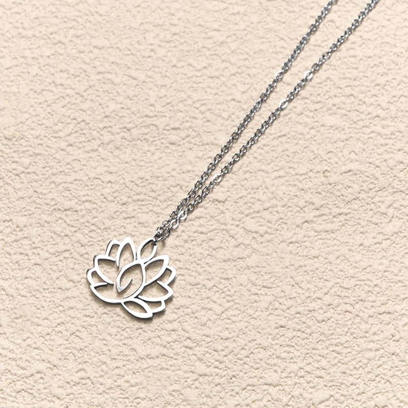 Lotus pendant necklace side flat lay view on textured beige background, silver-toned metal with thin chain design