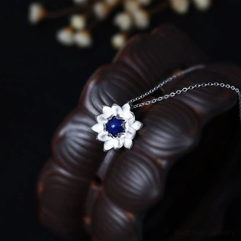 Miniature lotus silver pendant necklace with lapis lazuli, side angle view showing delicate silver-blue craftsmanship on wooden ring background