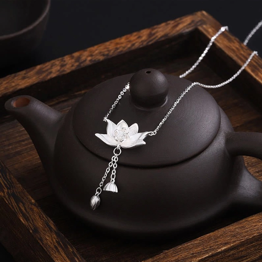 Buddhist lotus pendant necklace displayed on traditional wooden tea tray with clay teapot, showing authentic styling