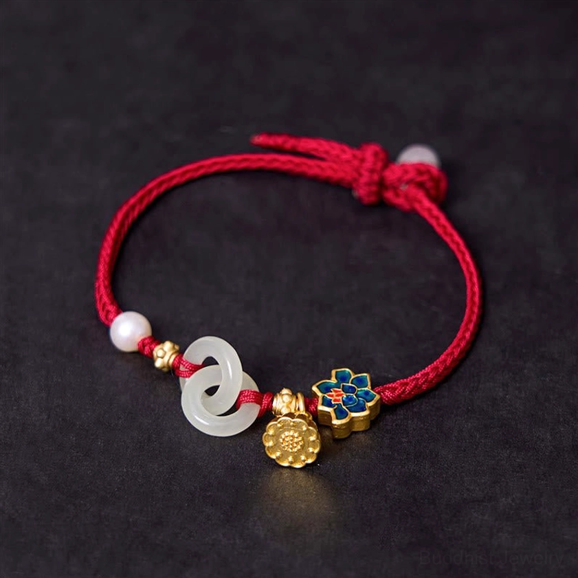 Buddhist fortune bracelet featuring gold lotus pendant, white pearl, enamel flower charm, and red braided rope on dark background