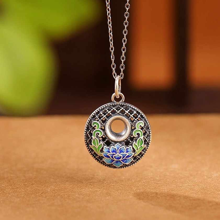 Silver lotus peace buckle pendant with cloisonne enamel lotus and leaf motifs filigree frame on tabletop