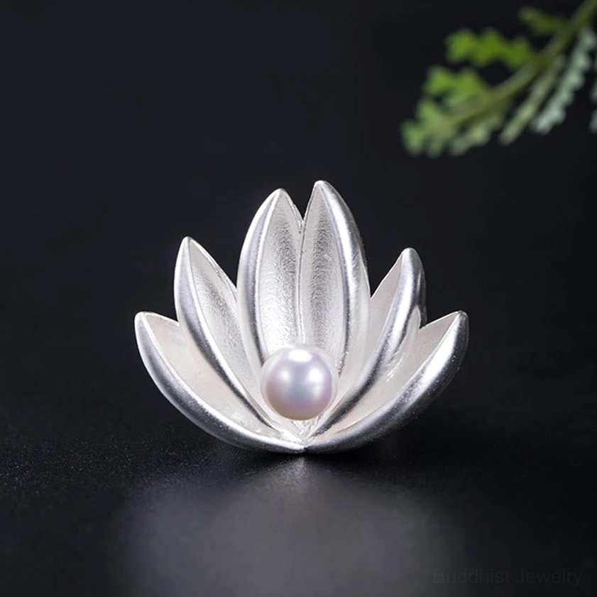 Front flat view of matte finish sterling silver lotus brooch with white pearl on black backdrop with green foliage accent