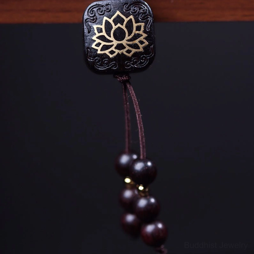 Detailed view of engraved lotus pendant with gold detailing and wooden tassel beads on mala bracelet