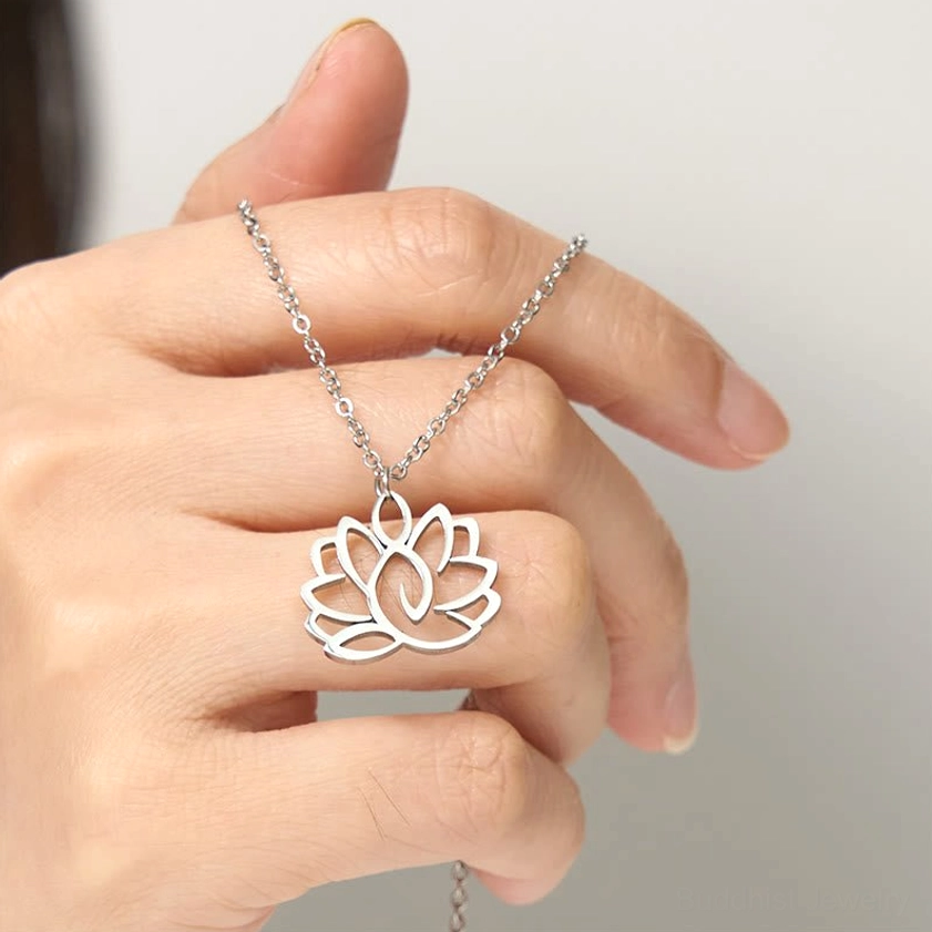 Hollow lotus pendant held in hand close-up, silver metal finish on plain indoor background showing scale and wear comfort