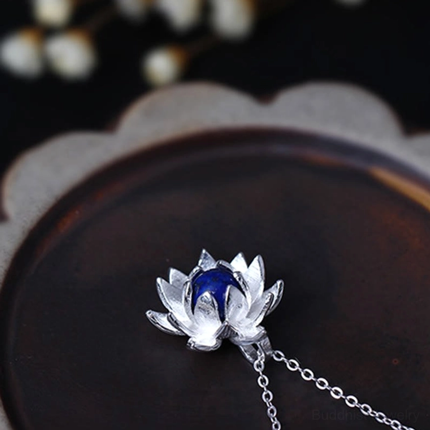 Lapis lazuli lotus flower silver necklace pendant, side angle view with thin silver chain, gem-set lotus design on dark wooden craft background