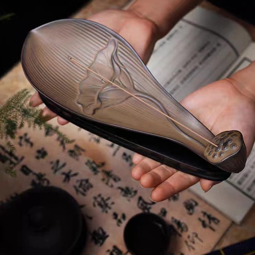 Close-up hand-held view of ceramic lotus incense burner with thin incense stick, lotus flower embossment detail