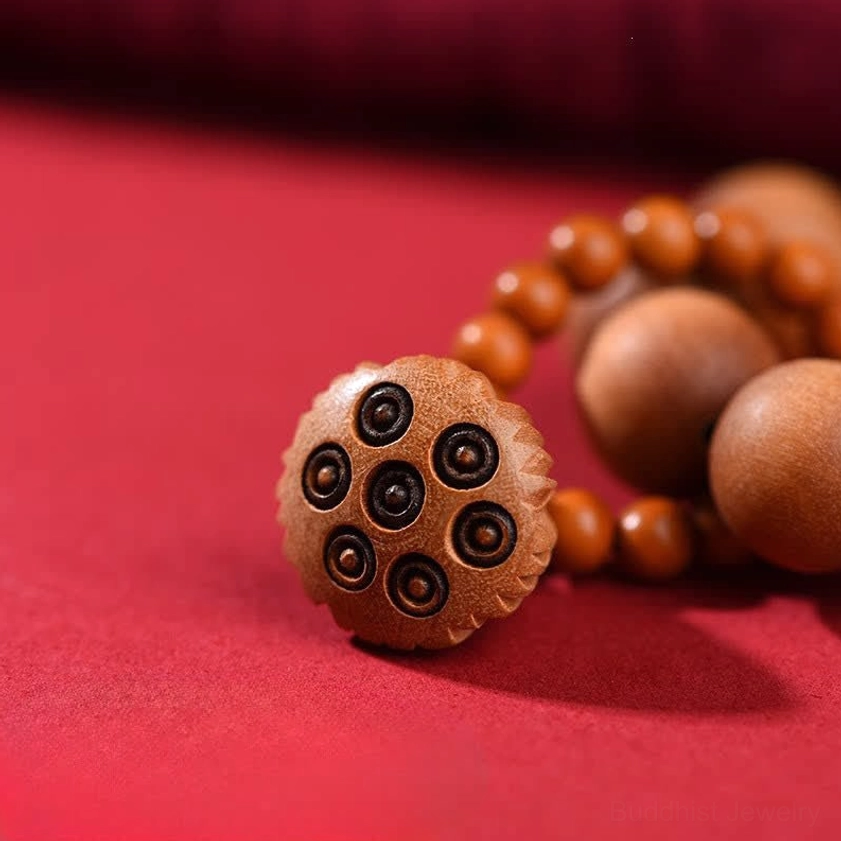 Macro close-up of carved lotus pod charm with intricate hole patterns and peach wood round beads showing fine natural wood grain detail