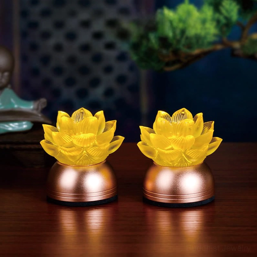 Pair of matching lotus prayer lamps with yellow liuli glass lotus tops and rose-gold copper bases displayed on wooden table indoors
