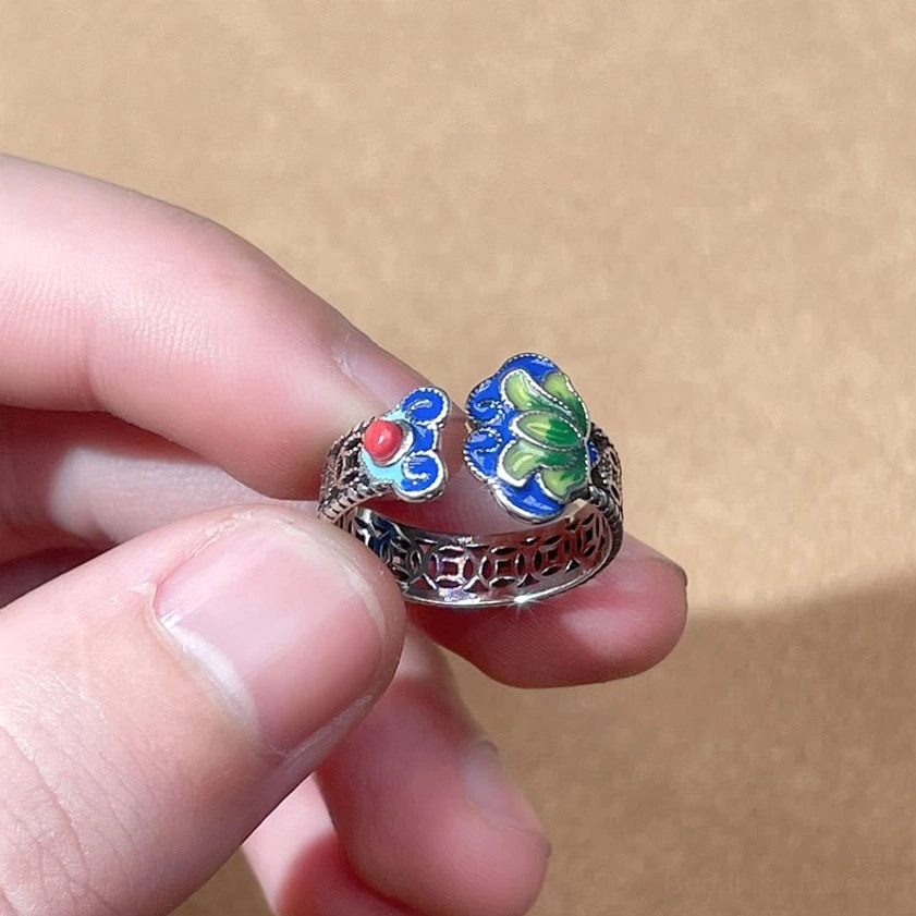 Close-up of adjustable open lotus ring held by finger displaying intricate cloisonne decoration