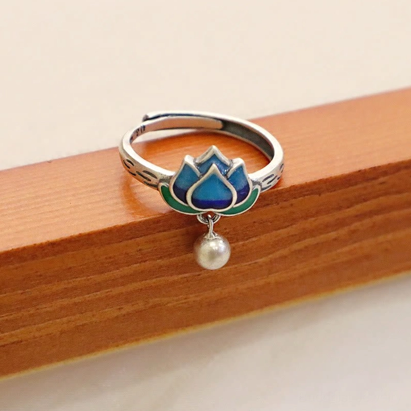 Cloisonné lotus silver ring placed on light wood surface showing smooth band with white pearl pendant and blue-green enamel lotus flower