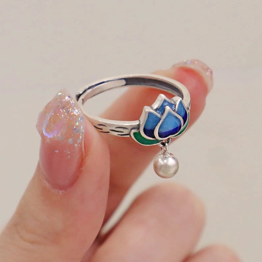 Lotus enamel silver ring held in hand showcasing detailed blue cloisonné lotus petals, engraved band, and silver bell accent