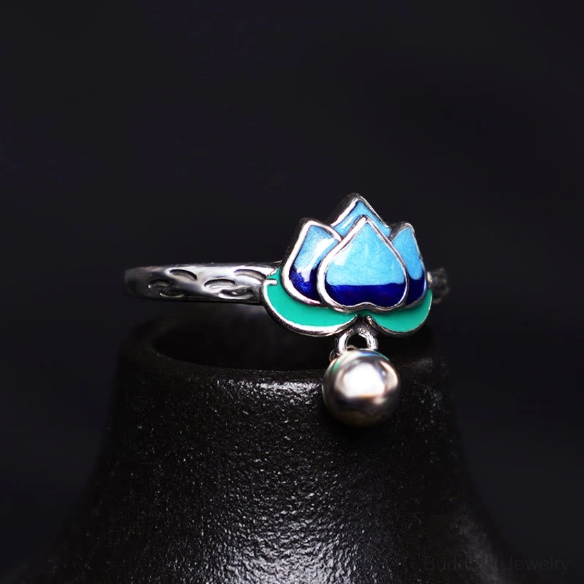 Lotus enamel silver ring with blue-green cloisonné design and dangling silver bell, displayed on black ceramic stand showing intricate engravings