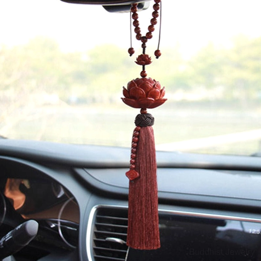 Red sandalwood carved lotus pendant with beaded tassel hanging in vehicle interior near air vent