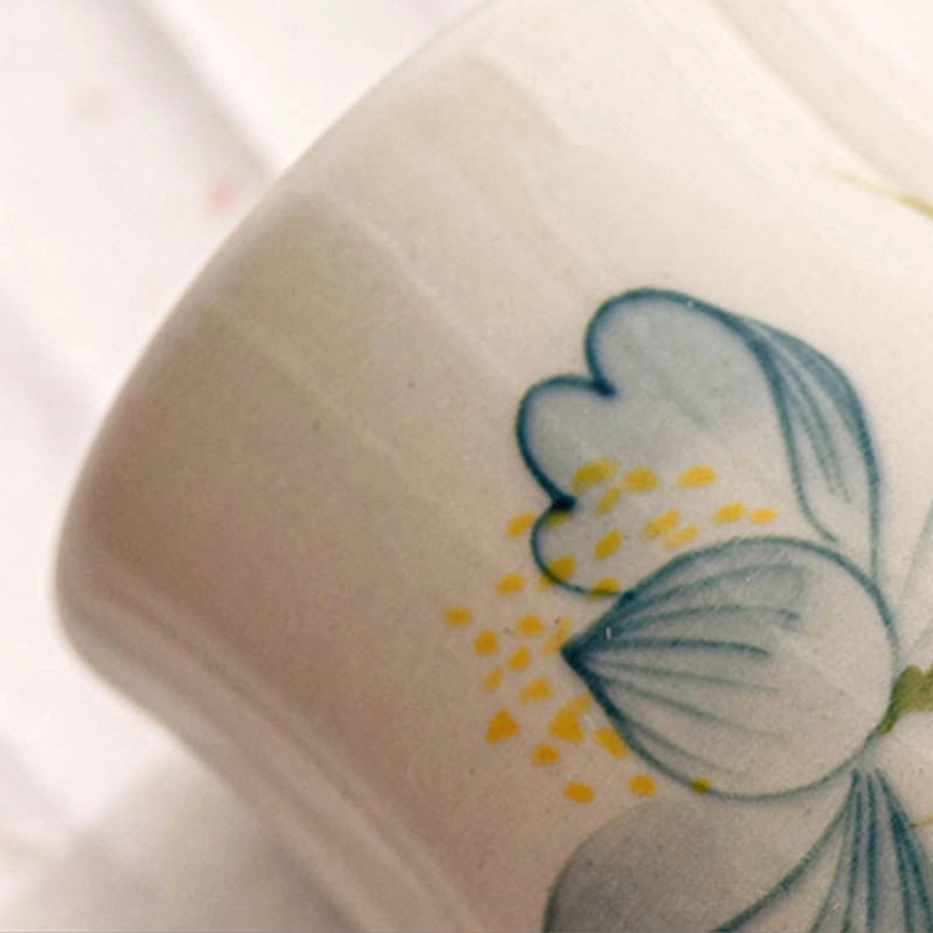 Close-up side angle of hand-painted lotus ceramic cup showing artistic brush strokes and flower details