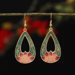 Teardrop lotus enamel drop earrings in green and red with gold metal trim, hanging on twig with floral background