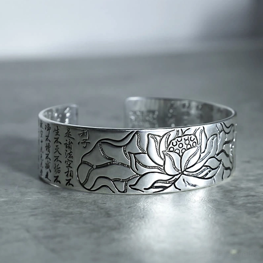 Lotus patterned white copper open cuff bracelet side 3/4 view on dark background with vertical sutra engravings and artisanal craftsmanship