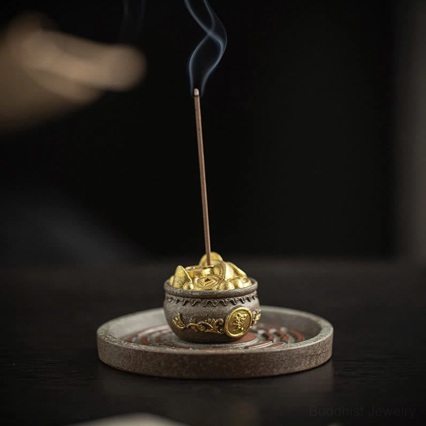 Low three-quarter view of small lucky bag ceramic incense burner with gold treasure decoration and lit incense