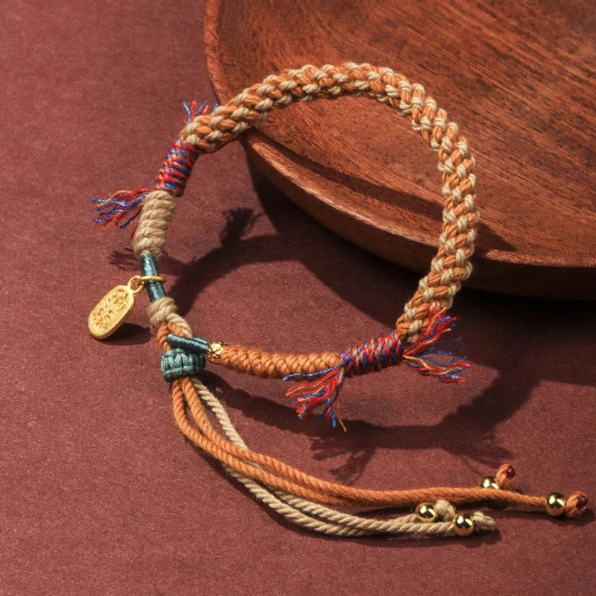 Overhead angled view of handmade multicolor braided luck bracelet with decorative tassels and long adjustable cord ends