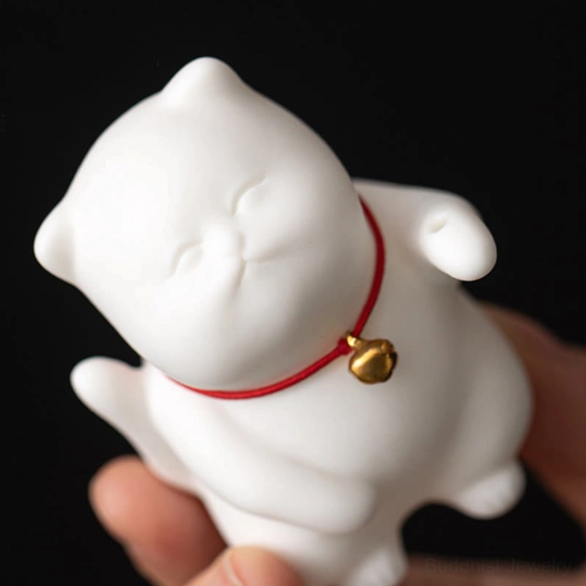 Close-up of white lucky cat figurine with red collar and brass bell held in human palm, eye-level view