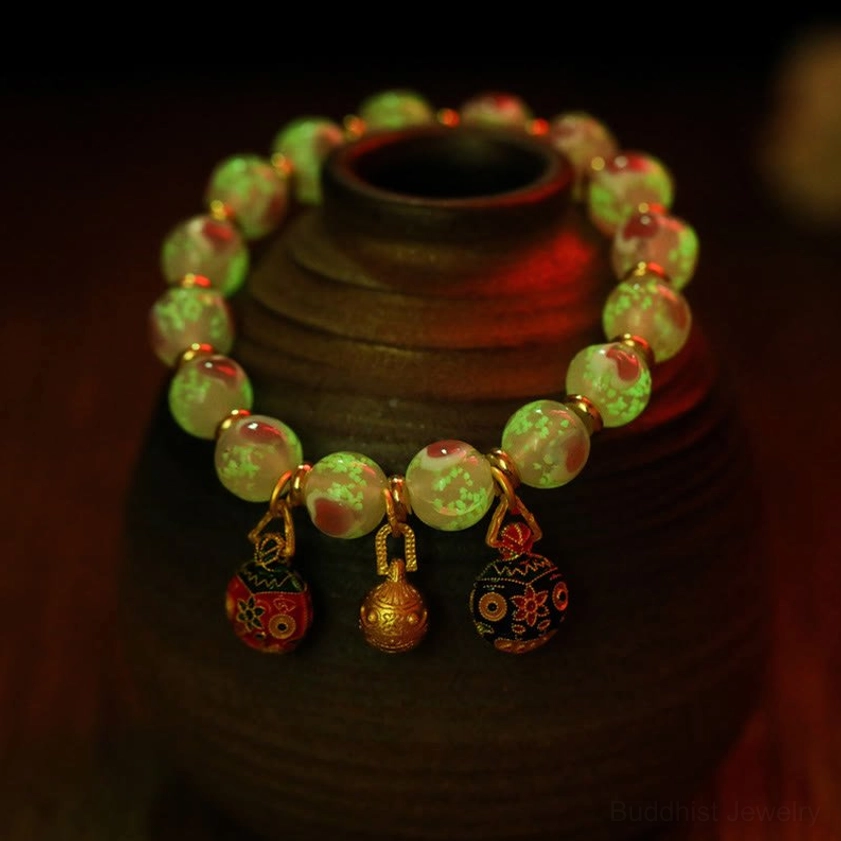 Luminous green glow-in-the-dark glass bead Buddhist bracelet with enamel metal pendants in close-up view with ceramic jar background