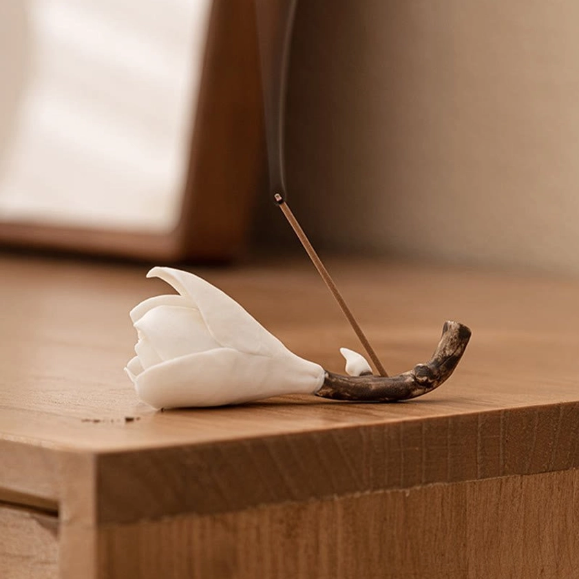 Ceramic magnolia incense holder with burning incense on light wooden desk creating minimalist Buddhist meditation ambiance