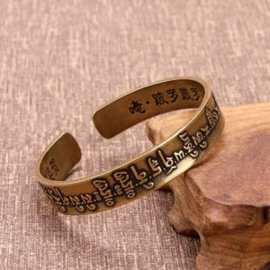 Mahapratisara Sanskrit mantra brass open cuff bracelet on wooden stand with linen fabric background showing engraved mantras