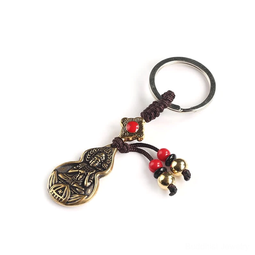 Flat lay product photography of bronze gourd Buddha keychain on light background showing complete design with red beads, golden bells, silver key ring, and braided tassel cord