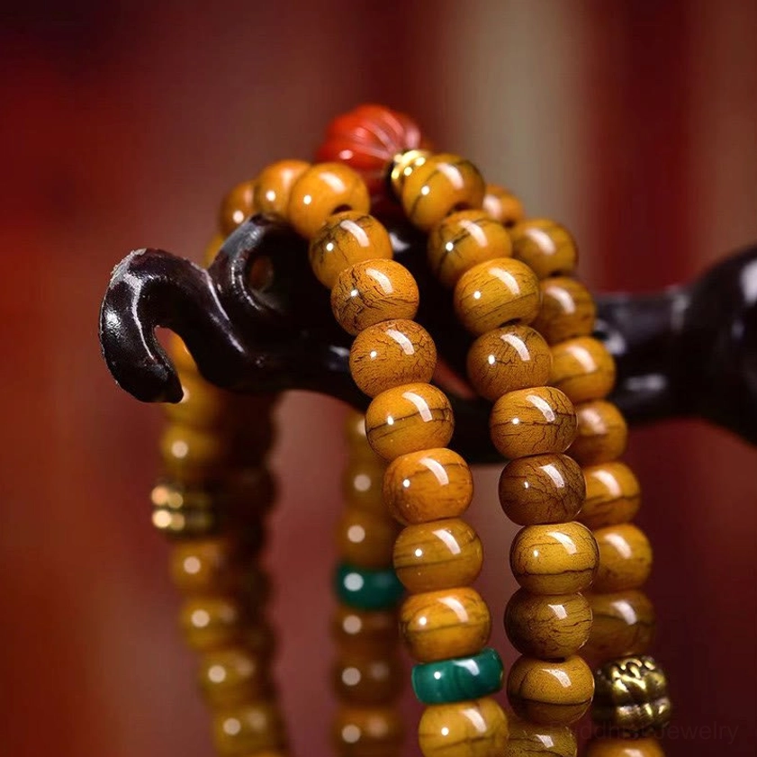 Close-up macro detail of Buddhist prayer mala beads showing smooth tan bone barrel beads, turquoise spacer, red accent bead, and silver metal hardware