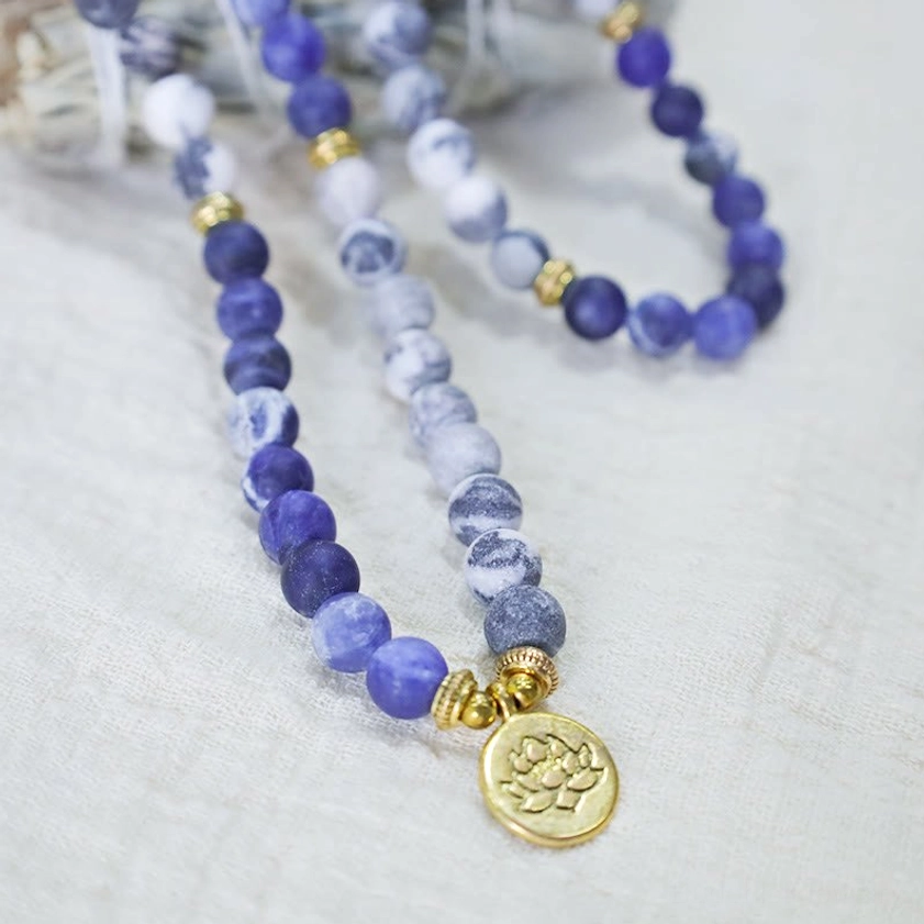 108 bead Picasso Jasper mala necklace with lotus charm, flat lay on linen fabric displaying gradient blue stone beads
