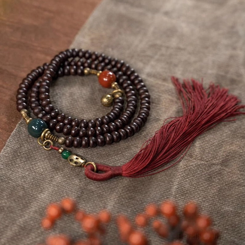 Close-up overhead view of 108 Bodhi Seed Mala with scattered red accent beads, dark round prayer beads, and long red tassel