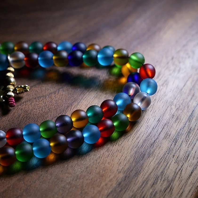 Partial strand of colorful mala beads with round frosted glass beads and metal clasp charm, side angle close-up view