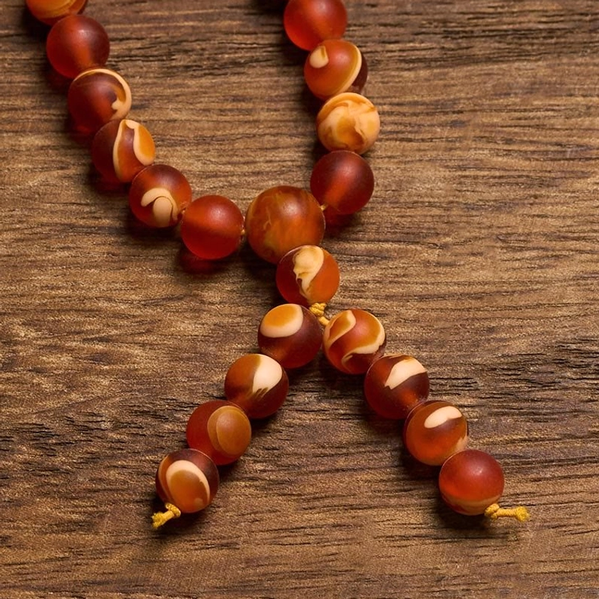Close-up detail of amber mala beads showing texture and yellow cord tassel on wood