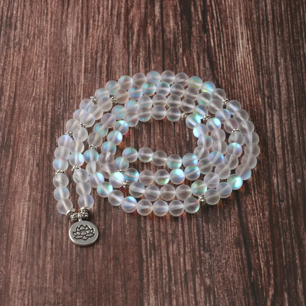 Flat lay of 108 glitter stone mala bracelet with shimmering frosted round beads and metal lotus charm on dark wood grain surface