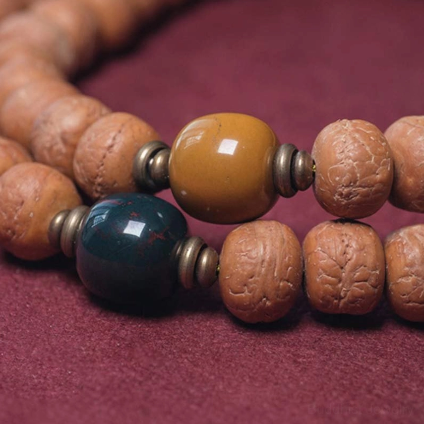 Close-up of decorated mala beads showing colored glazed accent beads, metal spacers, and natural Bodhi seeds