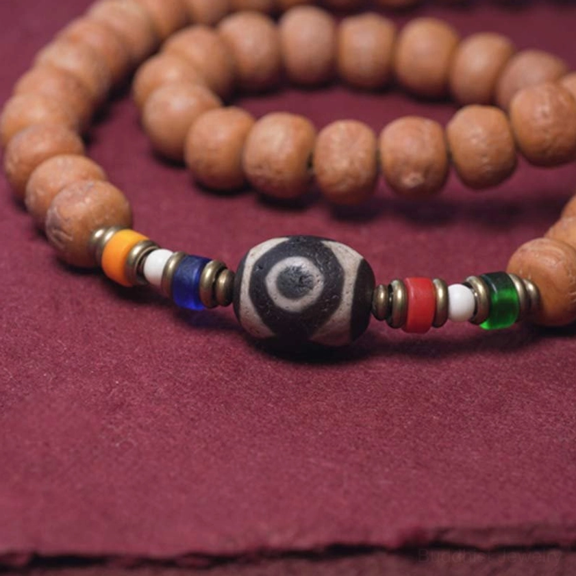 Close-up detail of 108 mala bead assembly showing Dzi bead with eye pattern, metal spacers, and natural seed beads