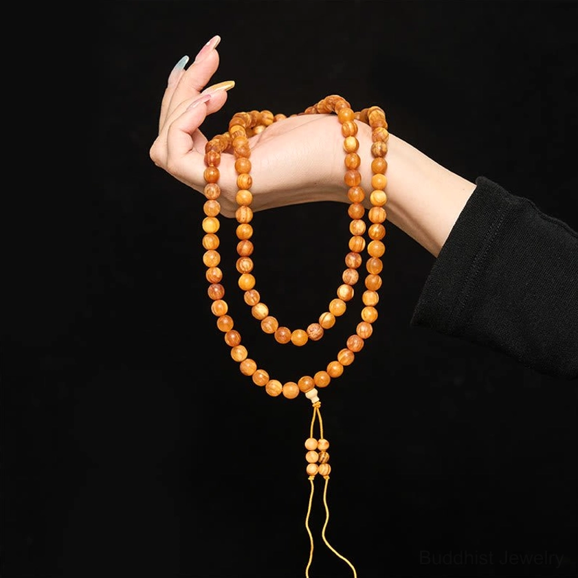 Double-loop resin-rich pine wood mala beads held by hand on black background, wrist prayer beads style