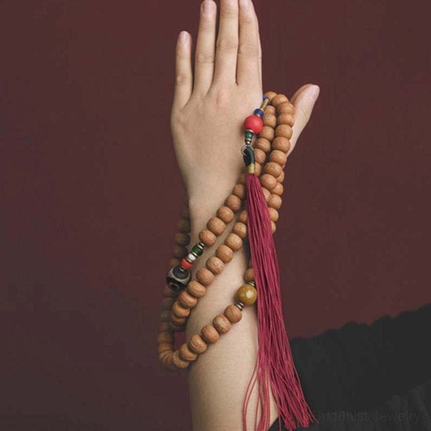 Hand holding 108 Bodhi seed mala beads showing close-up of natural seed beads, colorful spacers, and red tassel